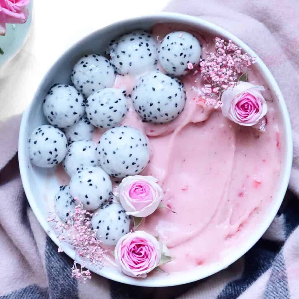 Strawberry, rose & oats breakfast smoothie bowl topped with dragon fruit balls and edible flowers