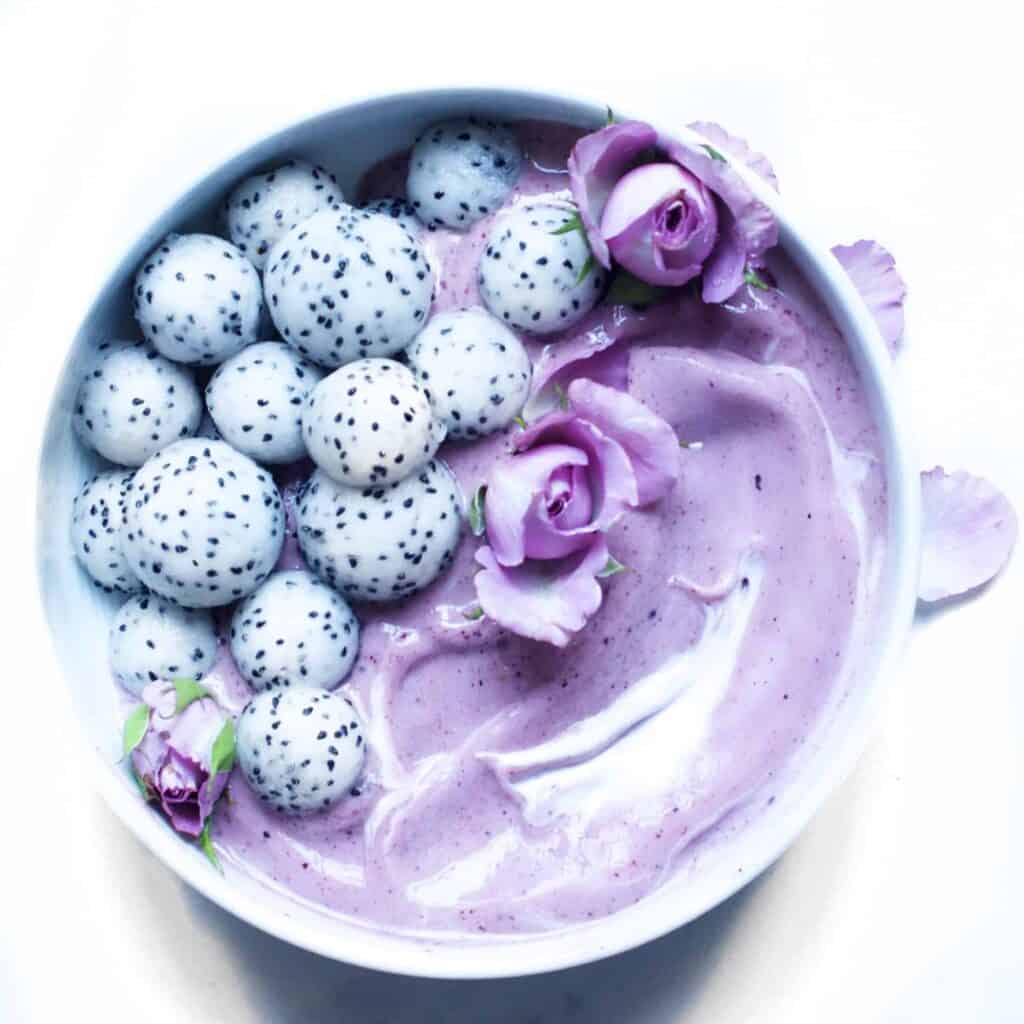 Blueberry and Acai Smoothie Bowl topped with dragon fruit balls and edible flowers