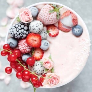 Pink smoothie decorated with frosted red fruit and edible flowers