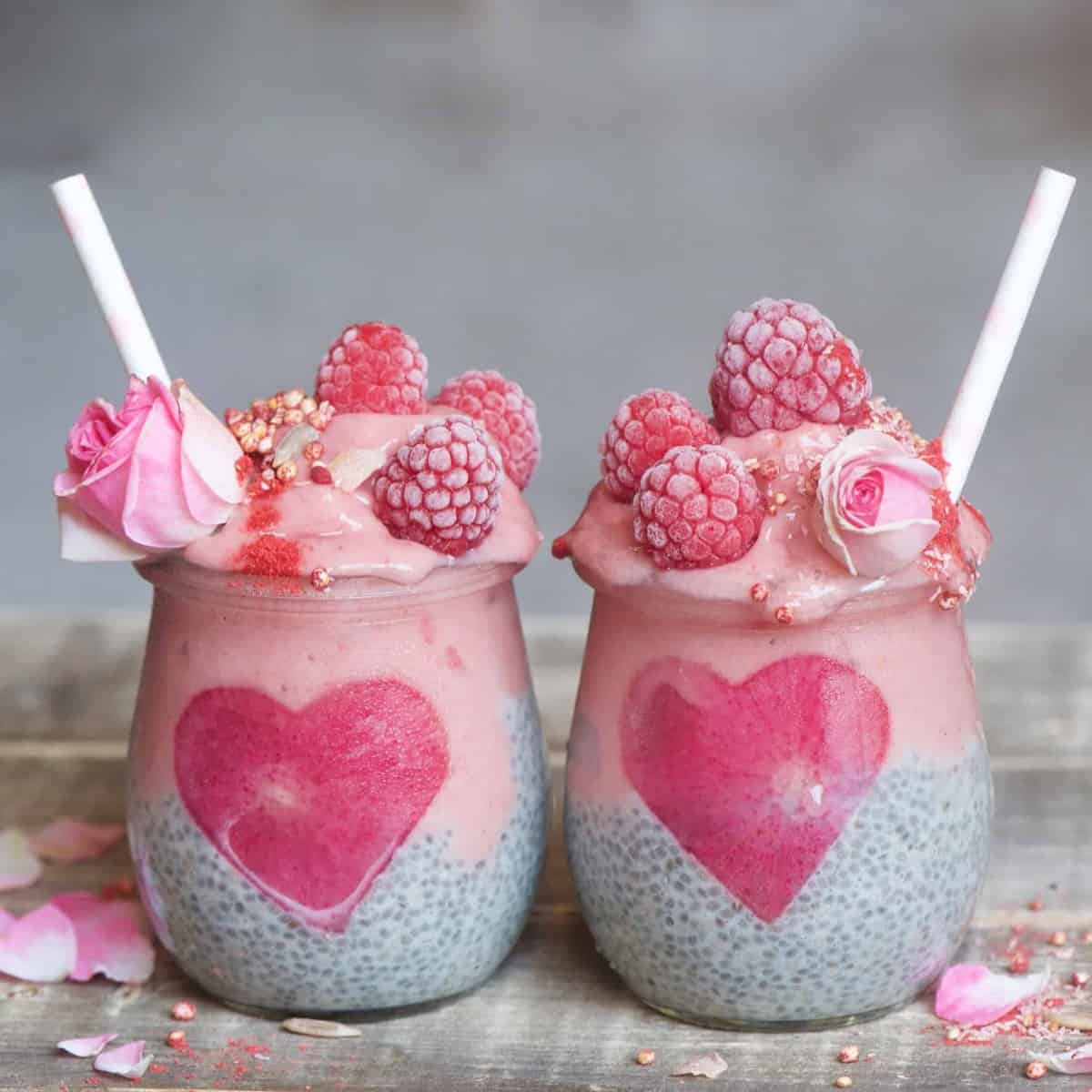 Two jars with chia pudding with pink yogurt decorated with raspberries and edible flowers 