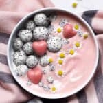 A bowl with pink smoothie with dragon fruit balls pink chocolate hearts and edible flowers