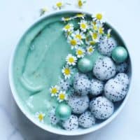 A bowl of spirulina mint smoothie with dragon fruit balls and edible flowers