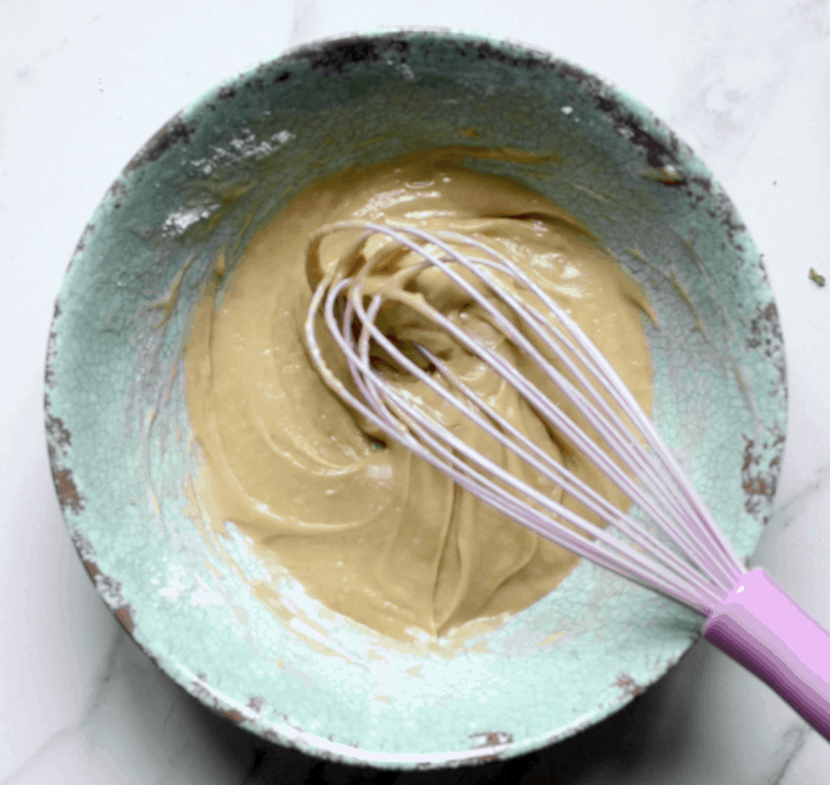 Waffle batter in a green bowl with a whisk 