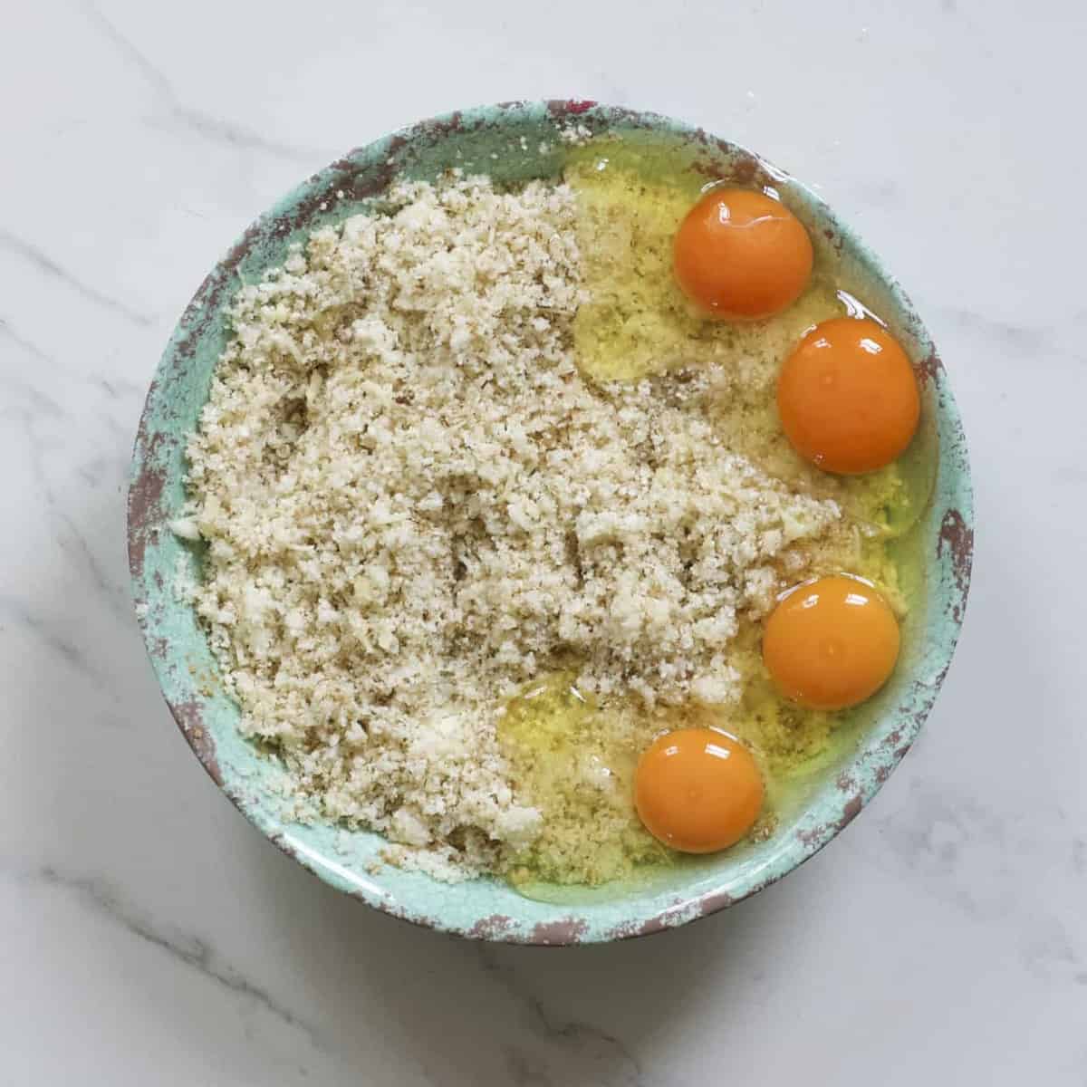 Mini pizzas base mixture and four cracked eggs in a green bowl