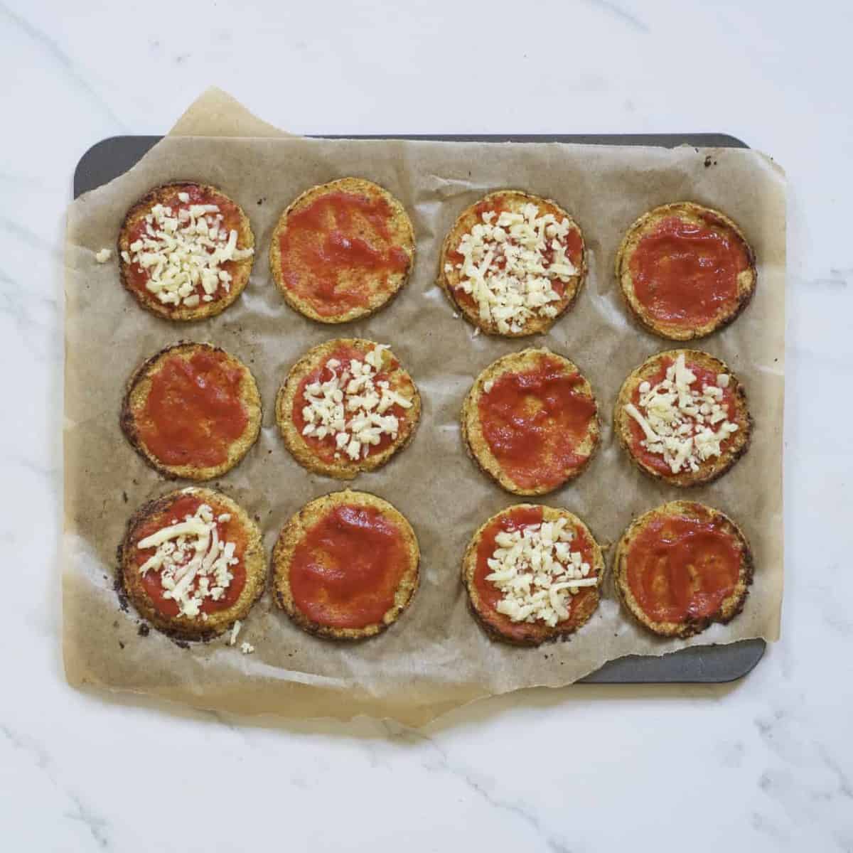 Baked mimi pizzas topped with tomato sauce and some with cheese on a baking tray
