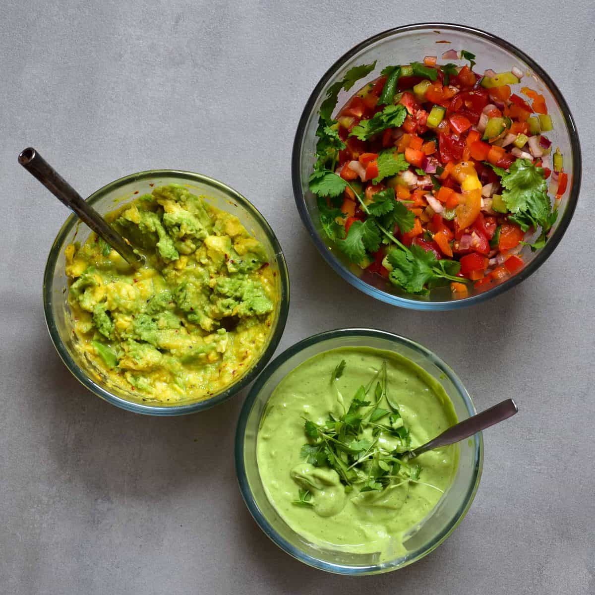 A bowl with pepper salsa, a bowl with guacamole and a bowl with green dipping sauce