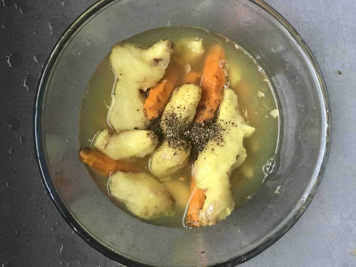 A bowl with peeled ginger and turmeric, lemon juice and some black pepper
