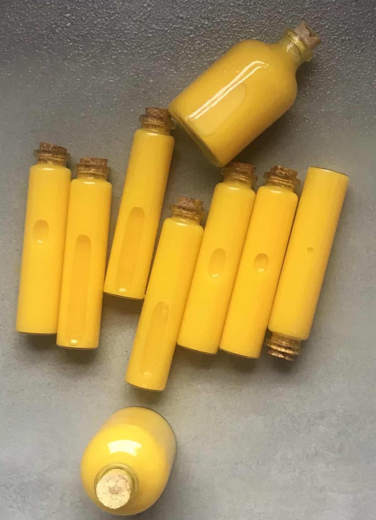 Nine small glass vials filled with turmeric and lemon shots laying on a flat gray surface
