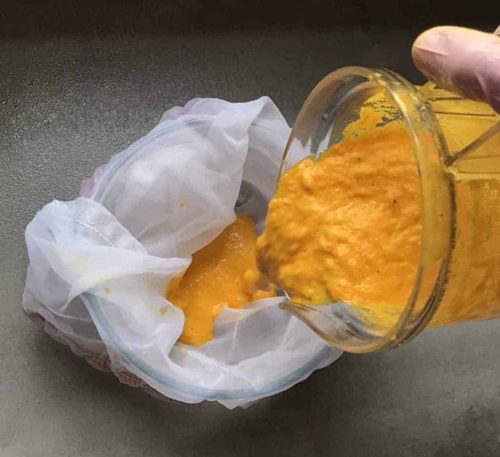 Sieving blended turmeric and ginger juice through a nut milk bag to called the pulp