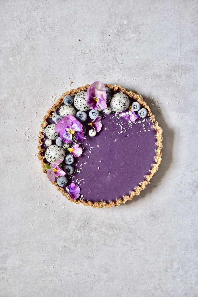 Blueberry tart decorated with dragon fruit balls and purple edible flowers
