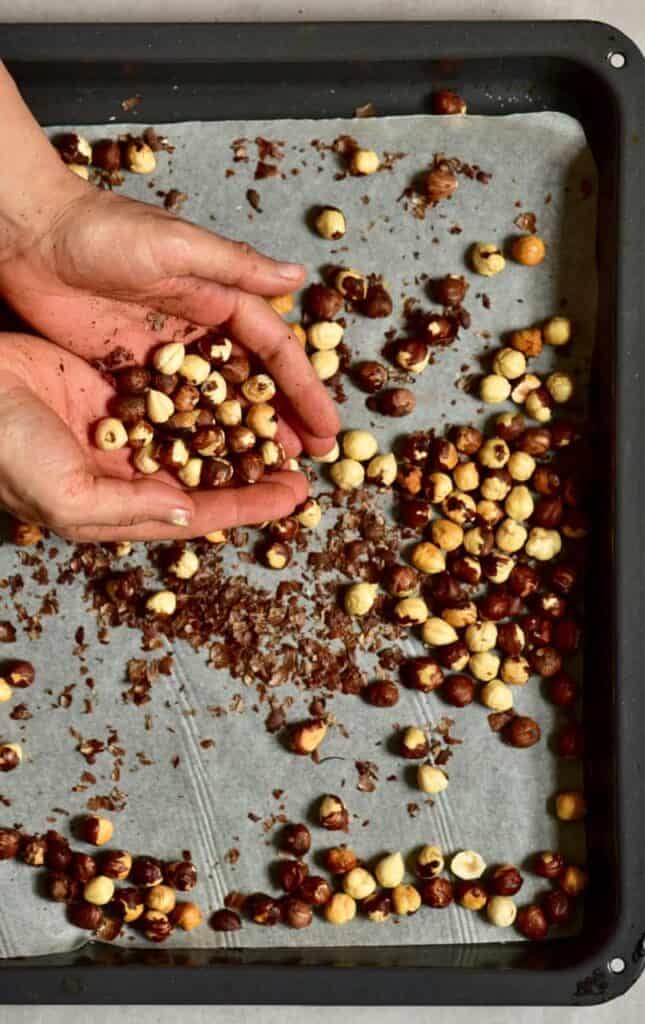 Roasted hazelnuts in a tray and a handful of roasted hazelnuts