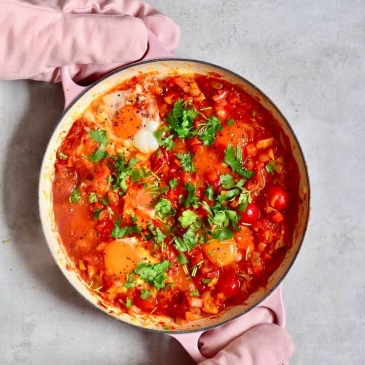 a pan of shakshuka with two hands holding it