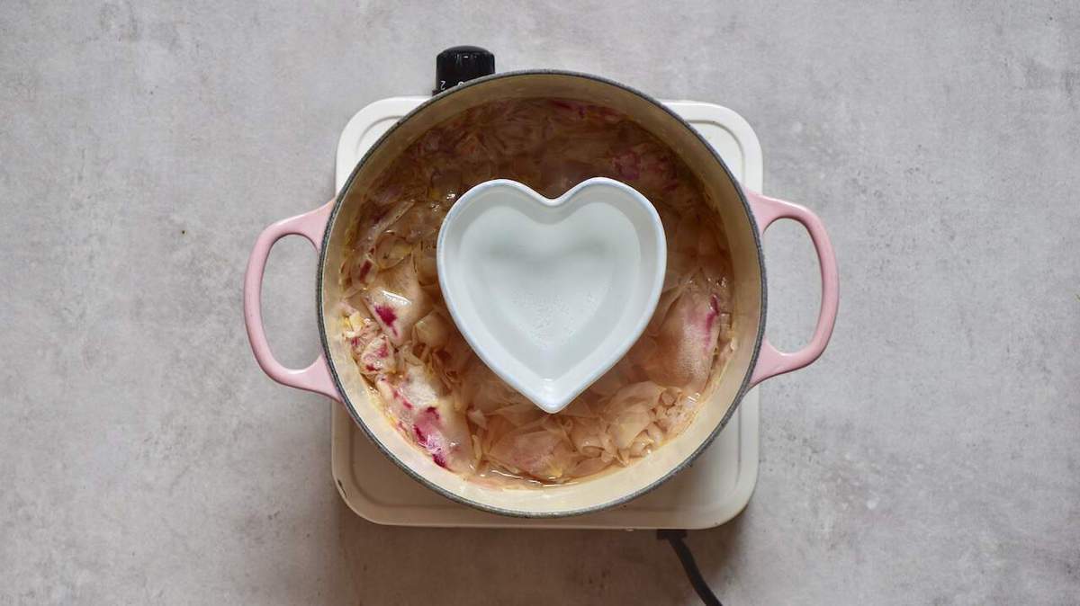 A heart shaped bowl filled with rose water in a pot with roses