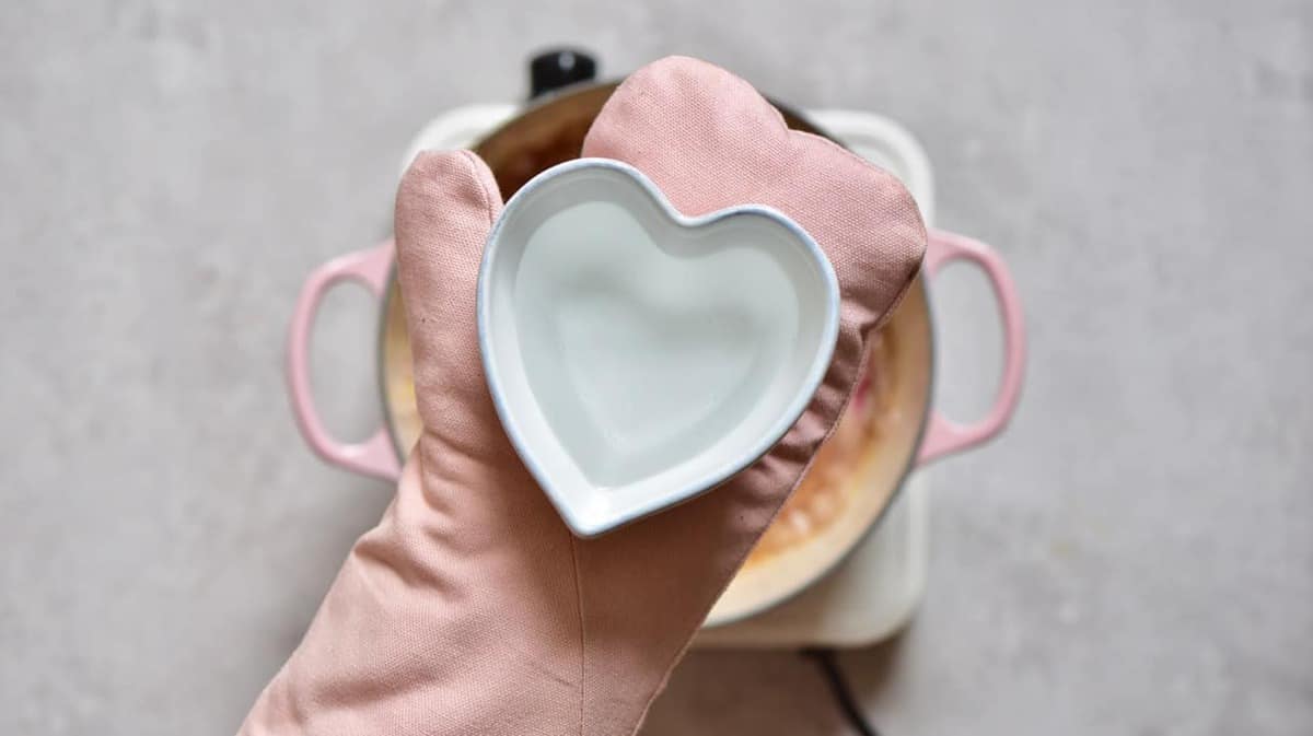A heart shaped bowl filled with rose water being held by a gloved hand