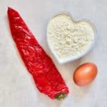 A heat shaped bowl with flour a roasted red pepper and an egg