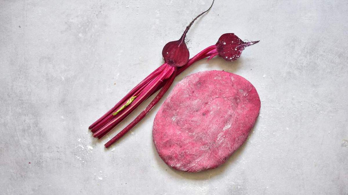 Red pasta dough and two halves of beetroot on a flat gray surface