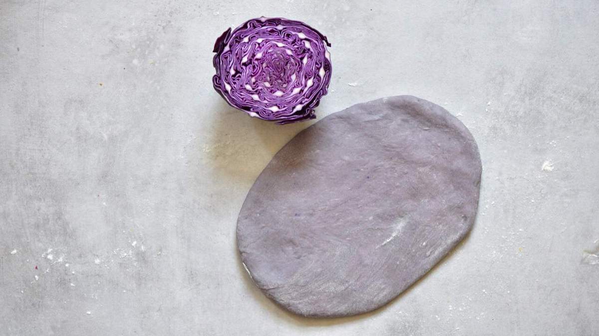 Purplish pasta dough and a half of red cabbage on a flat grey surface