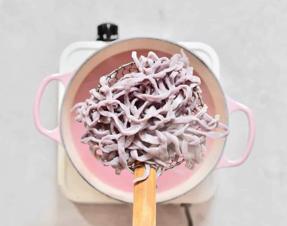 Homemade purple pasta in a colander spoon above a pot