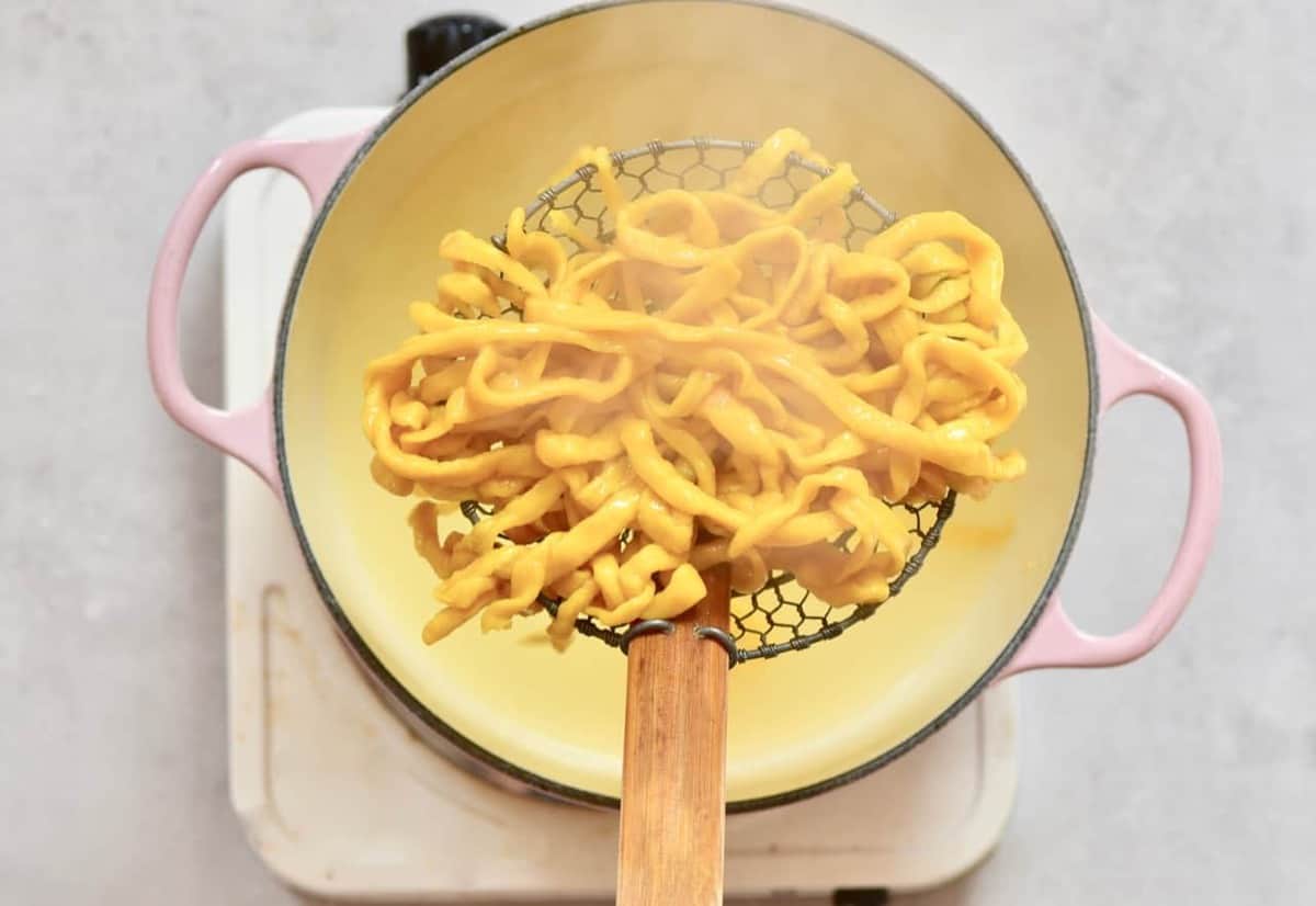 Homemade yellow pasta in a colander spoon above a pot