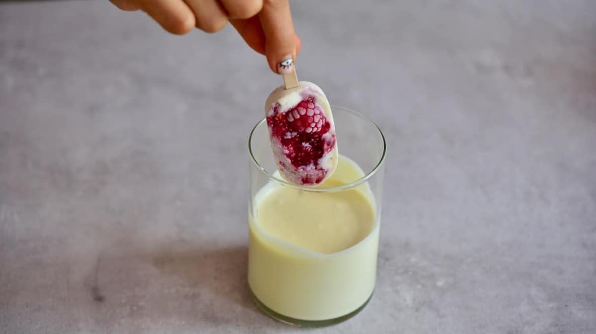 A homemade ice cream with raspberries being dipped in melted white chocolate