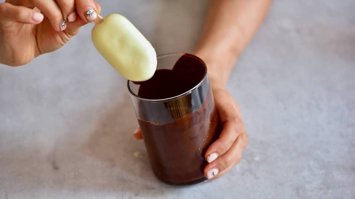 A homemade magnum ice cream being dipped in dark chocolate in a glass