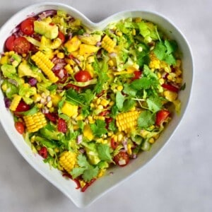 A big heart-shaped bowl filled with corn mango tomato and avocado salad