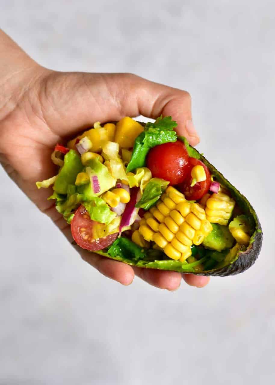 An avocado half filled with corn and tomato salad
