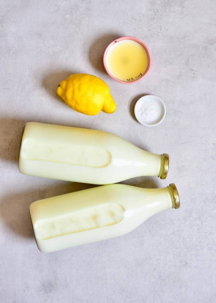 two bottles of milk, a lemon, and salt on a plain background