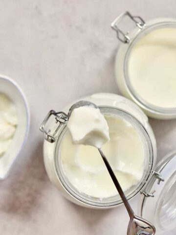 A spoonful of homemade natural yogurt placed on top of an open jar and another jar with yogurt next to it