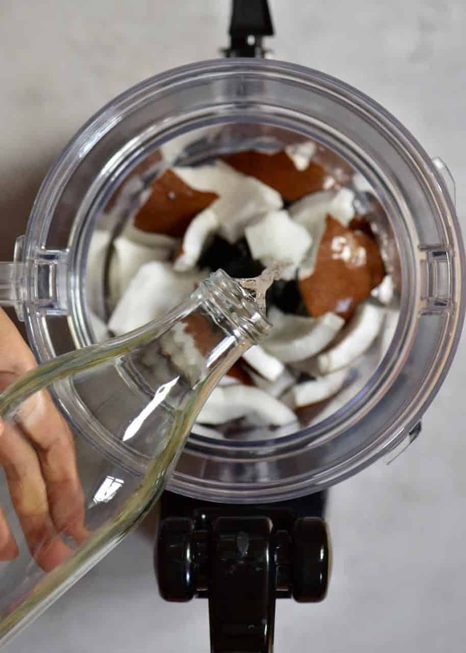 pouring water into food processor which has coconut meat