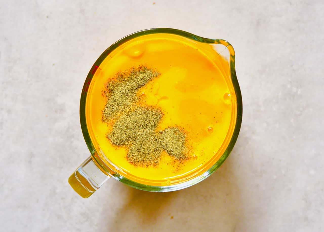 A large measuring cup with turmeric and ginger juice and black pepper