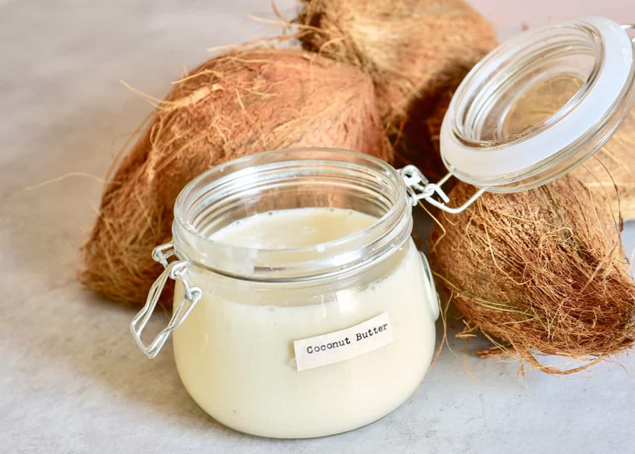 coconut butter jar with mature coconuts next to it 
