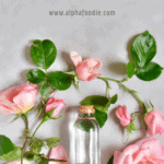 A vial with homemade rose water placed flat on a gray surface and surrounded with pink roses 