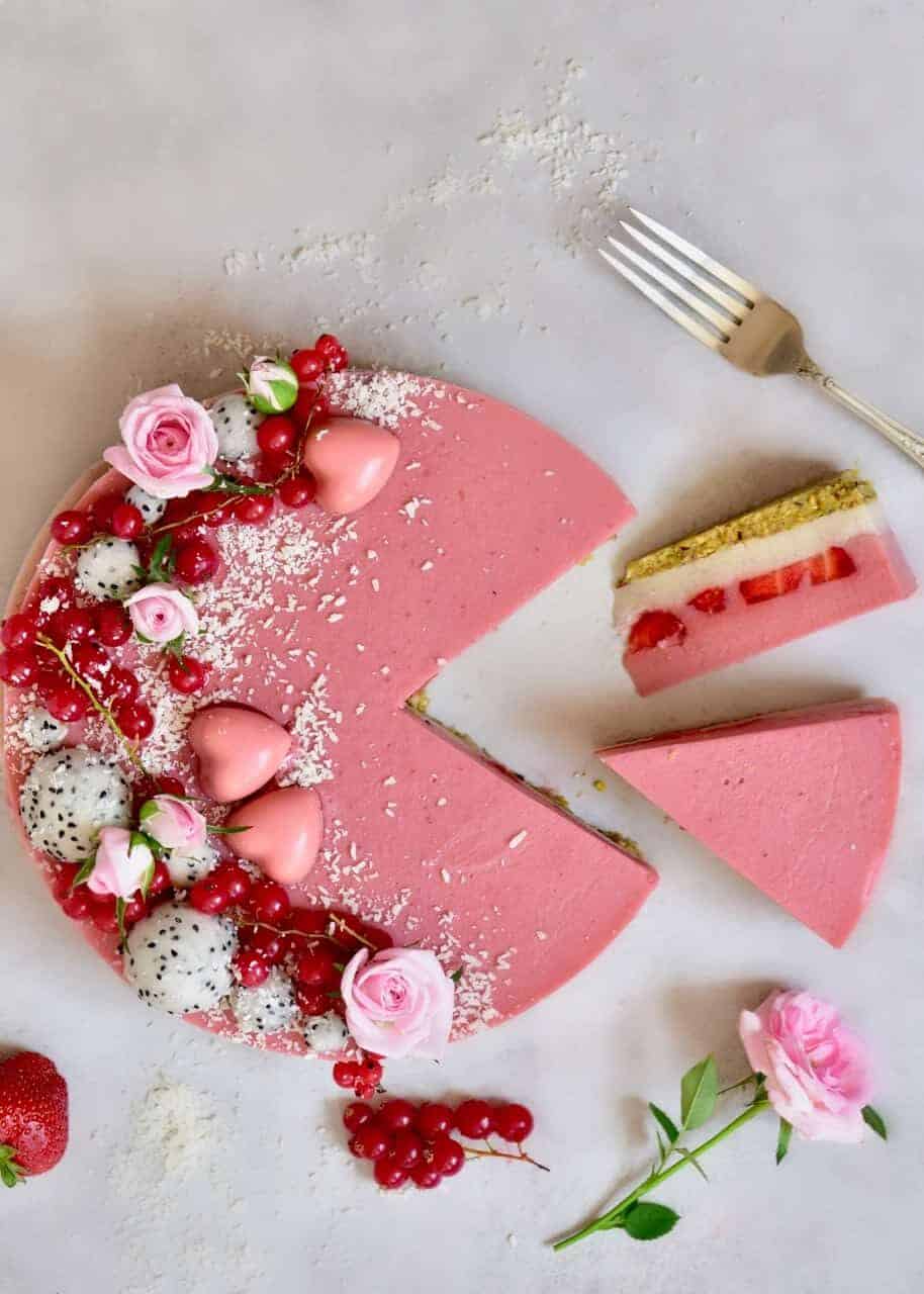Layered strawberry tart decorated with red berries and dragon fruit balls with two slices cut off