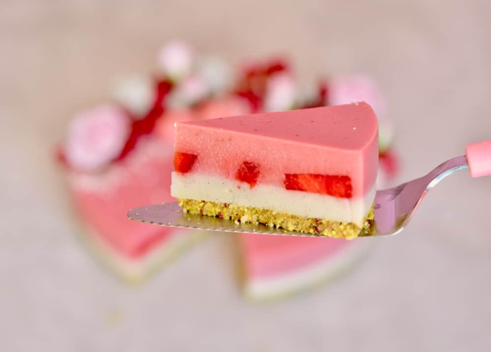 a side view of a slice of Two-layer Vegan strawberry tart with a pistachio & Almond crust and coconut & strawberry layered filling with fresh strawberries.
