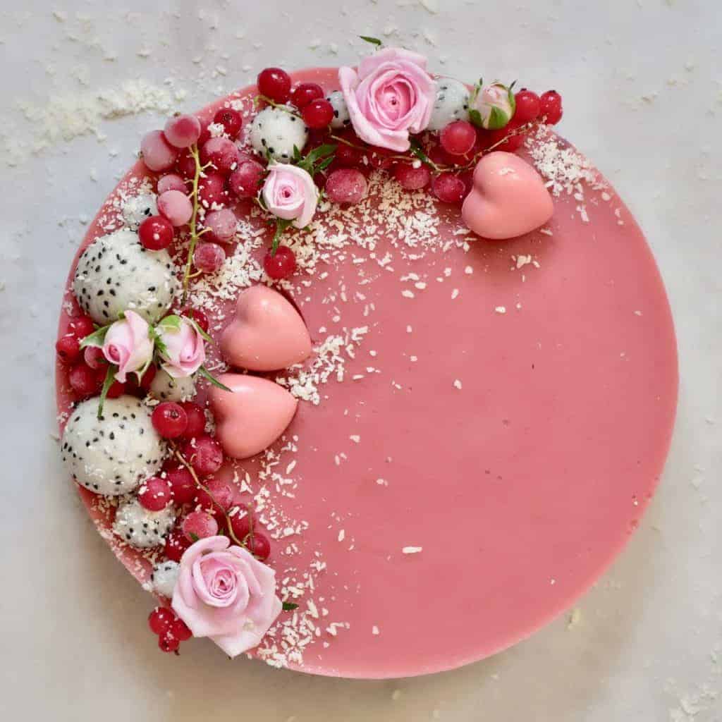 two-layered coconut and strawberry tart topped with coconut, dragon fruit, red berries and edible roses
