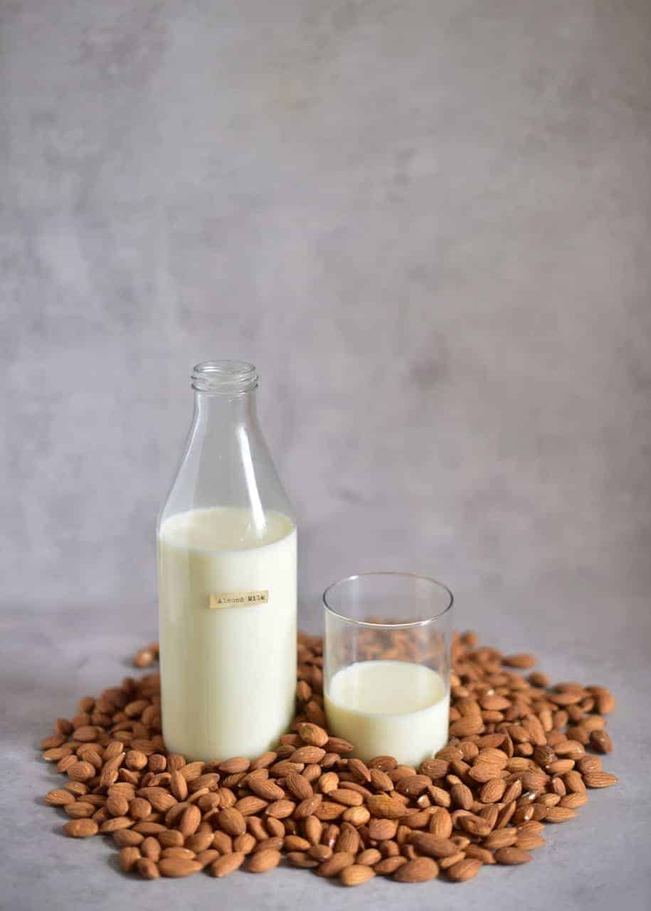 homemade almond milk in a bottle and poured in a glass with almonds on the surface 