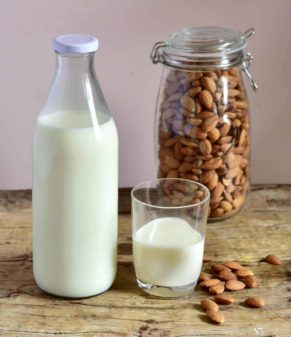 homemade almond milk poured in a glass with the bottle and jar of almonds behind 