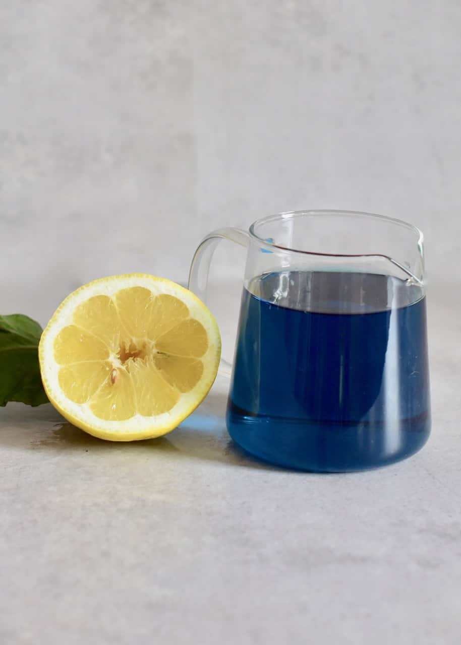 jug of concentrated butterfly pea tea next to half a lemon