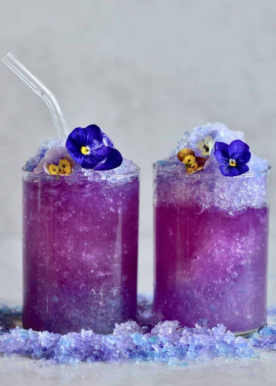 Two glasses filled with magic colour changing lemonade with blue pea flower tea and edible flowers.