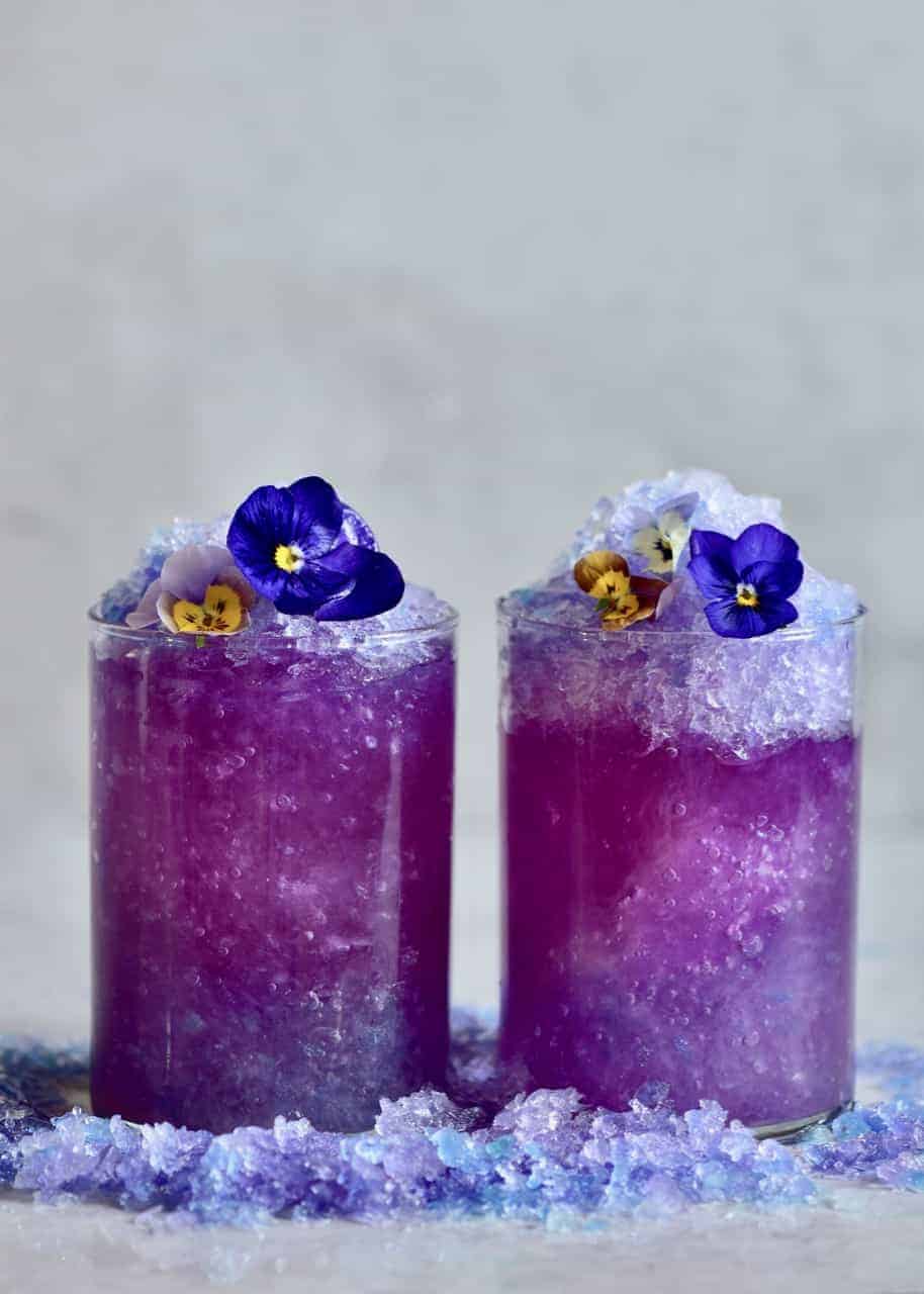 two glasses of butterfly pea flower lemonade with crushed ice and edible flowers 