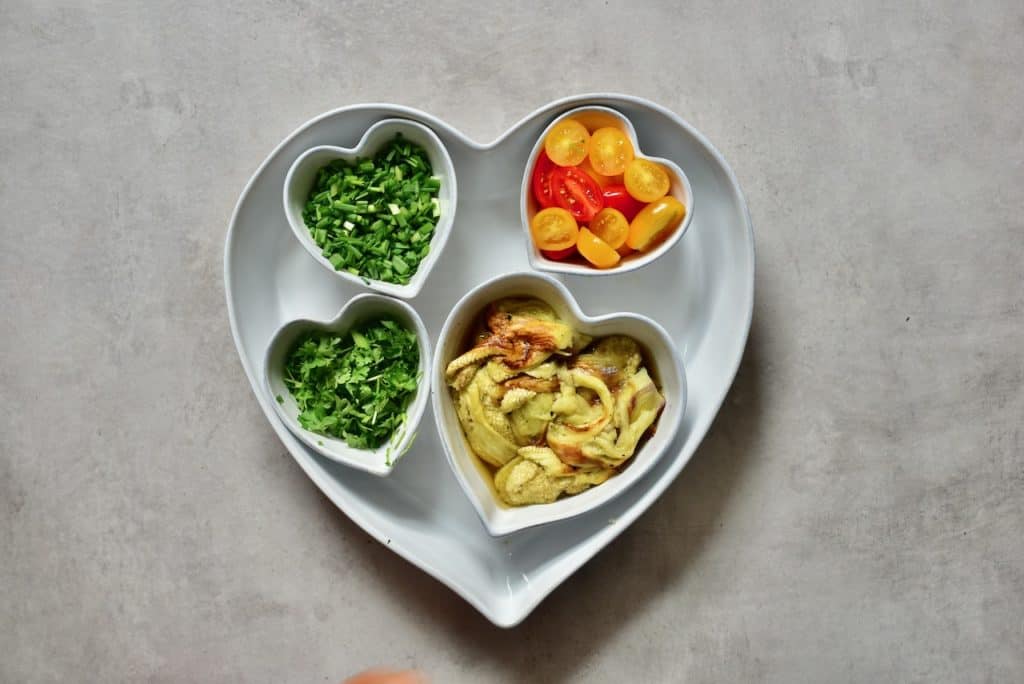 various salad ingredients in small heart-shaped tubs. tomato, herbs. green onion and aubergine