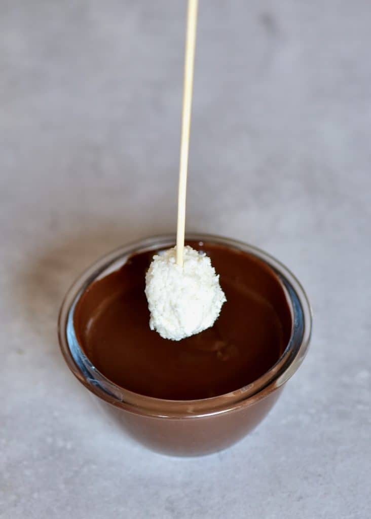 dipping a coconut ball in dark chocolate 