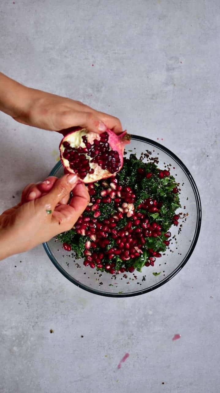 Opening a pomegranate over a quinoa kale salad