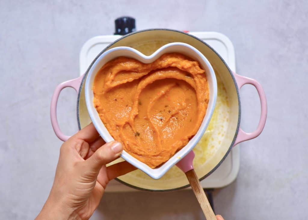 homemade pumpkin puree being added to coconut curry pumpkin soup. vegan