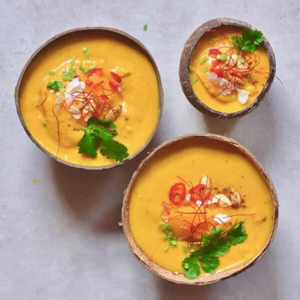 Three little coconut bowls filled with pumpkin curry soup topped with chili and parsley