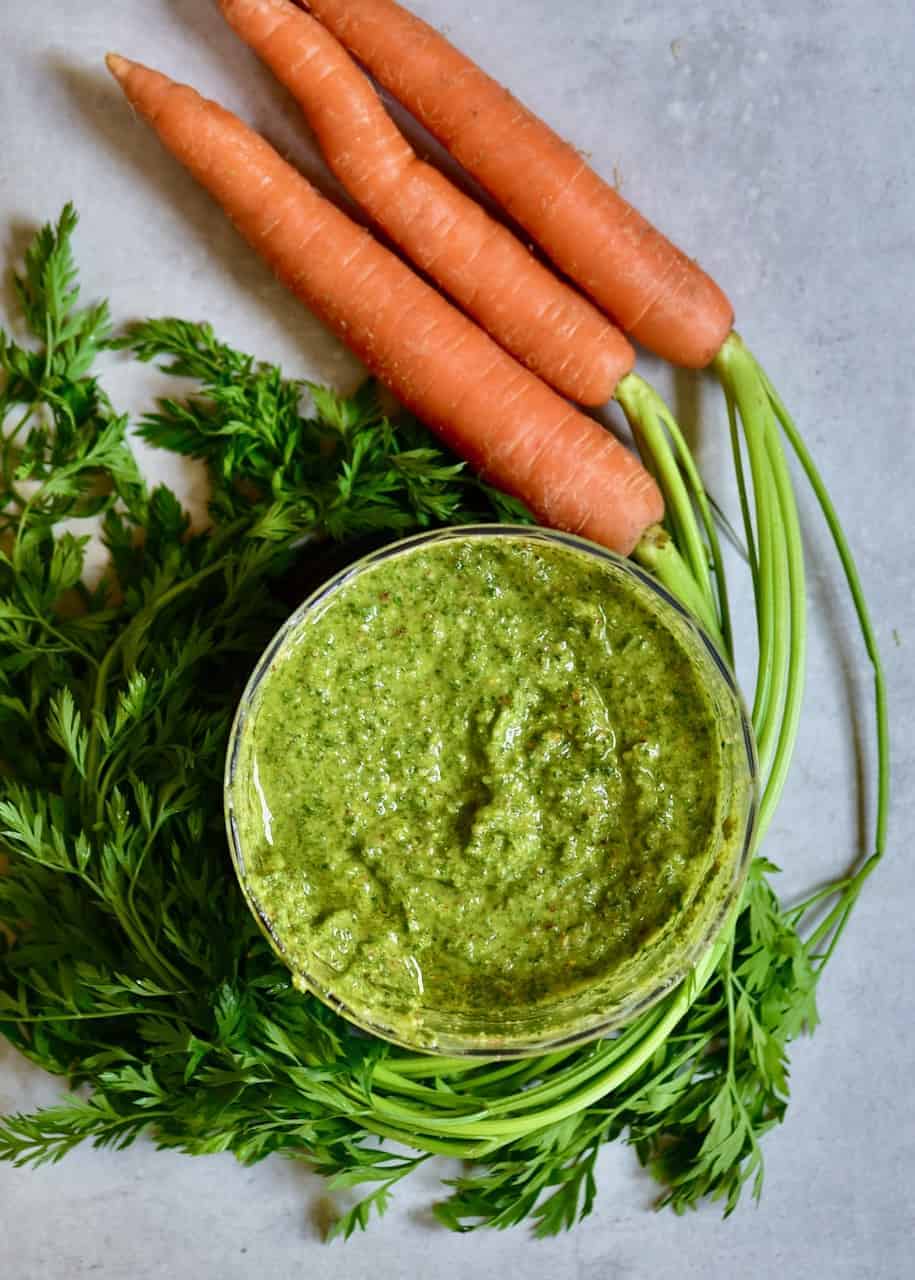 Carrot top pesto in a small blender and three carrots next to it