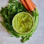 A small bowl with carrot pesto and carrots with tops around it