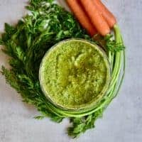 A small bowl with carrot pesto and carrots with tops around it