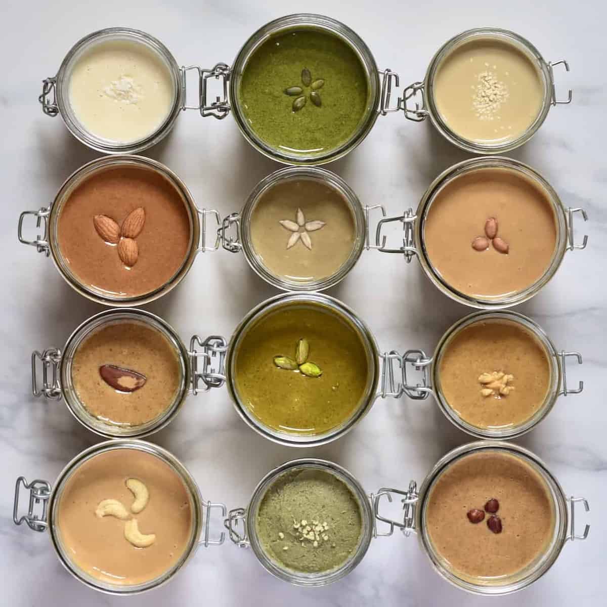 Twelve jars filled with different types of seed and nut homemade butters